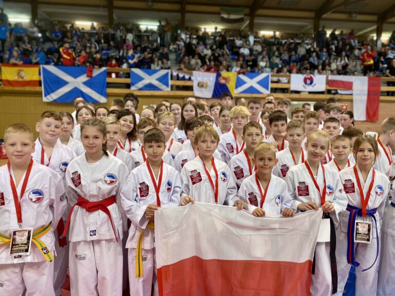 Duża grupa młodych zawodników Polskiej Federacji Taekwon-Do z polską flagą na międzynarodowym wydarzeniu